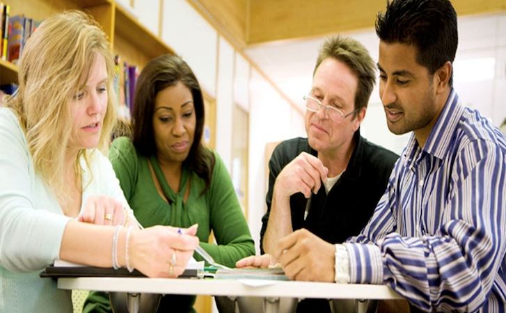 Four people sitting around a table in a library engaged in a study session Four people sitting around a table in a library engaged in a study session
